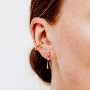 Close-up of an ear with gold earrings on a plain background
